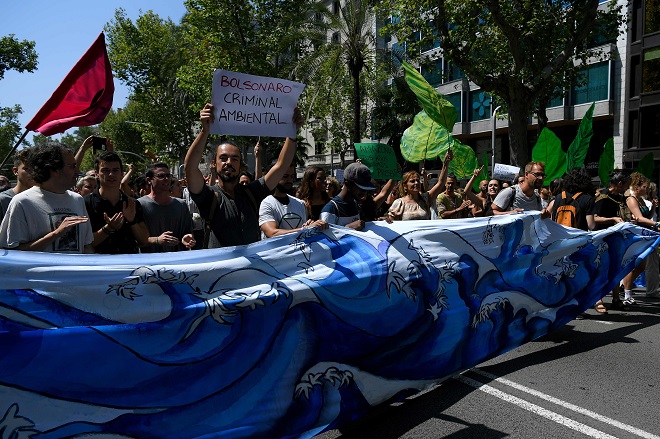نشطاء المناخ يحملون لافتة كتب عليها (الرئيس البرازيلي جير) بولسونارو هو مجرم بيئي أثناء مسيرتهم خلال مظاهرة في برشلونة ضد حرائق الأمازون